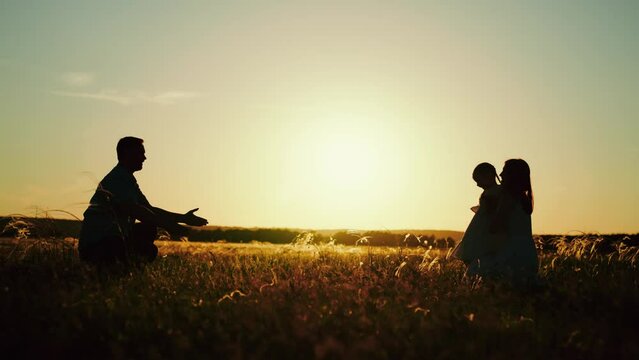 Parents with child playing after delightful picnic on nature in field at sunset. Parents hugging daughter on summer holiday. Parents with daughter go to vacation to spend time in family circle