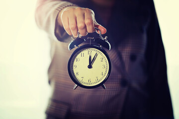 A young woman in a stylish suit holds an alarm clock in her hands. The concept of the end of the...