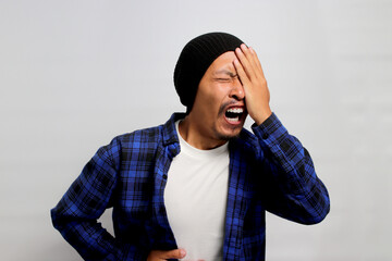 Funny Asian man is yawning and covering half of his face seemingly experiencing sore eyes. He might...