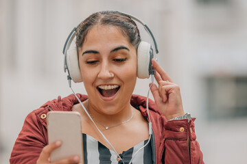 girl with headphones smiling looking at mobile phone surprised