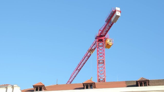Red construction crane moves against a blue sky. Construction crane over the roofs of houses. Construction works