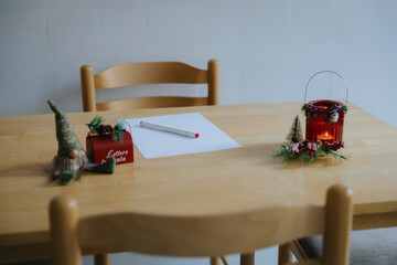 A sheet of paper, a pen and Christmas decorations on a wooden table.