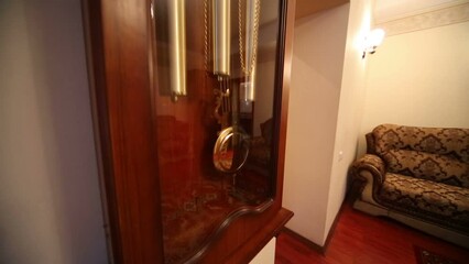 Big wooden wall clock with moving pendulum in living room