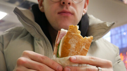 Close-up of a bitten sandwitch in the hands of a man sitting in a fast food restaurant
