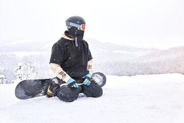 Shot of snowboarder that sitting with his snowboard on legs and looking for a ride moment