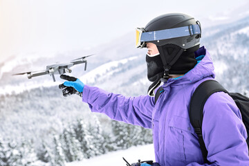 Male snowboarder with equipment and black backpack is launching a flying drone with a remote...
