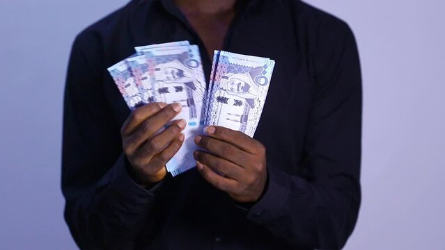 black male in black long sleeves shirt counting 500 Saudi riyal notes over white background