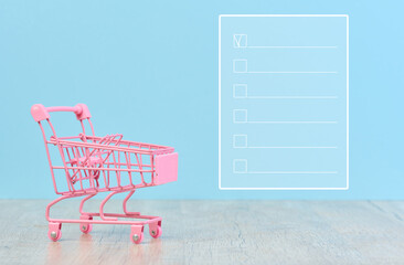 Miniature shopping cart and grocery shopping list on blue background