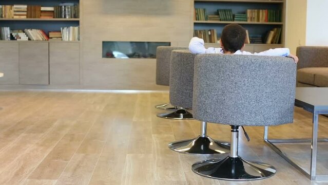 Cute mulatto boy in jacket turns in armchair in business center