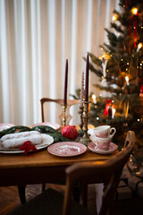 Christmas decorations, plates and candles with velvet bow, fir tree with christmas light bokeh