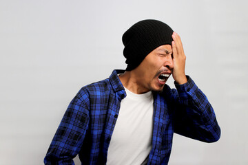 Funny Asian man is yawning and covering half of his face seemingly experiencing sore eyes. He might...