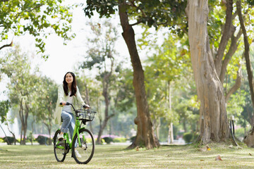 Happy asian woman riding bicycle on public park.