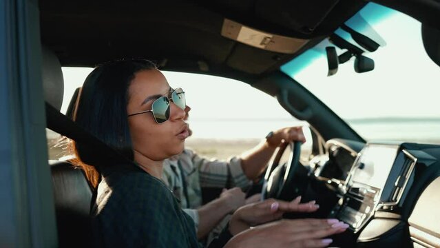 Positive multicultural young couple singing while listening to music in car in summertime