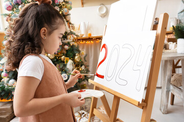 Talented schoolgirl artist paints red numbers 2024 on easel with palette and brush. Christmas tree...