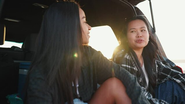 Concentrated multicultural female friends talking in trunk of car by estuary on sand in summertime