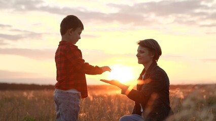 Son carefully gives hand to mother hugging in field with growing plants at sunset. Mother and son...