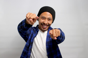An excited young Asian man is smiling warmly and pointing his finger towards the camera, indicating...
