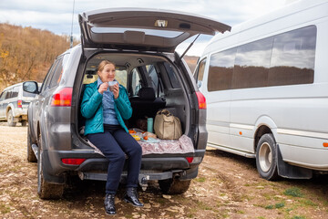 mature woman had a picnic in the trunk of her car. Road trip in the mountains in autumn