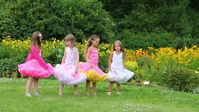 little girls in lush skirts hold hands and turn near flowerbeds