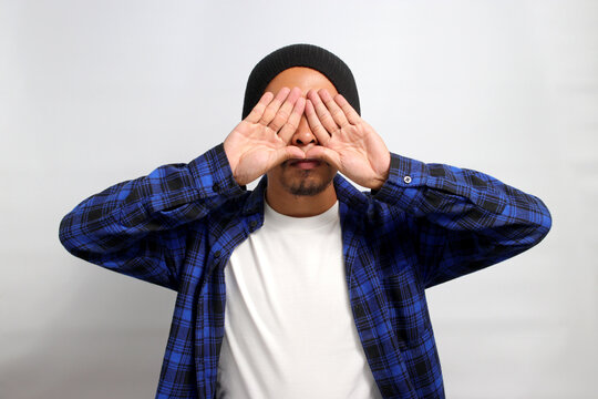 Young Asian man, dressed in a casual shirt and wearing a beanie hat, is creating a triangle shape with his hands, symbolizing the concept of environmental protection, recycling, and reusing