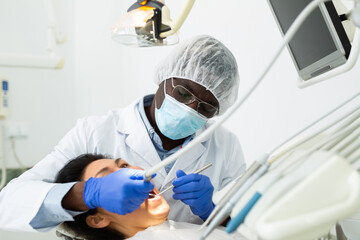 African american dentist professional filling teeth for woman patient sitting in medical chair