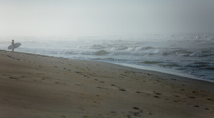 Surfer holding a surf board on the beach looking at the ocean. Depicting active outdoor adventure lifestyle