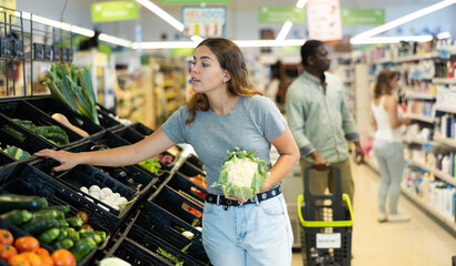 Positive young girl buying cauliflower at grocery market