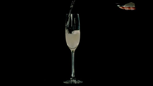 Champagne is being poured into the glass. Closeup of champagne pouring into the glass on a black background. Slowmotion, footage 4K. 