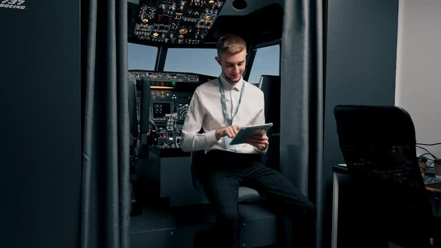 Portrait of an airplane captain or steward in uniform preparing for flight in flight simulator cockpit with tablet in hands