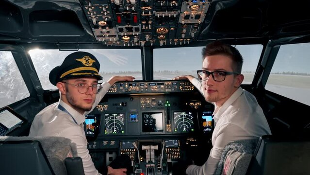 Portrait of serious young airplane pilot captains in uniform preparing for flight in flight simulator cockpit