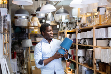 African American male shopper looking for table lamp and pendant light in household goods store....