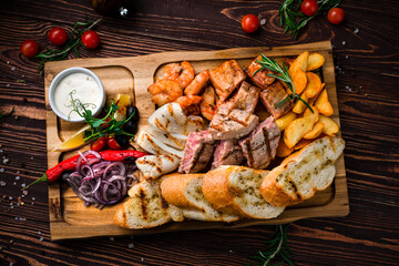 Fried shrimps, squid, tuna, salmon fillet, rustic fried potato wedges, onions, lettuce, chili peppers, toasts and sauce in a wooden board.