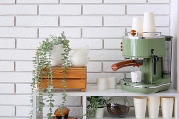 Modern coffee machine with cups and houseplants on shelving unit near white brick wall