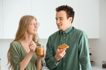 Young woman holding jar of nut butter and handsome man with toast in kitchen