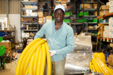African-american man working in warehouse, carrying rolled flexible tube.