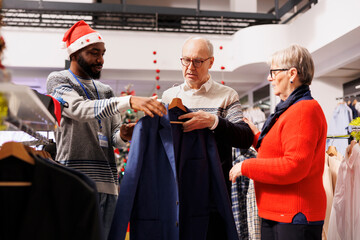 Man employee helping clients to choose jackets and blazers, making preparations for upcoming...