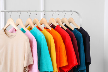 Rack with colorful t-shirts near light wall, closeup