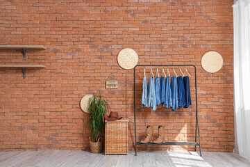 Rack with different jeans, shoes and houseplant near brick wall in boutique