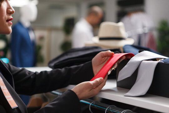 Shopping center boutique seller arms examining red tie while checking trendy accessory for sale on shelf closeup. Mall clothing store woman assistant hands exploring garment