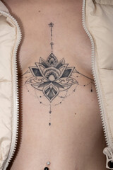 An intricate, symmetrical lotus-like tattoo adorns the upper chest, framed by an open textured...