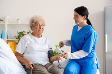 Female nurse measuring blood pressure of senior woman in bedroom