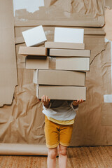 Unrecognizable little girl holding stack of boxes standing over craft paper cardboard background