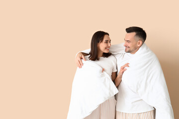 Young couple with soft blanket on beige background