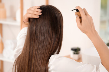 Young brunette woman applying hair product in bathroom, back view