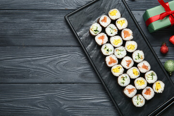 Board of tasty sushi rolls with gift box and Christmas balls on black wooden background