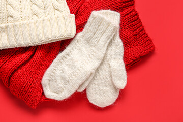 Pair of white knitted mittens with warm hat and scarf on red background