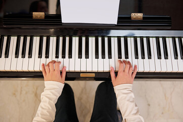 Top view of a child student, future musician pianist touching the white keys with his fingers,...