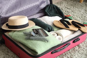 Suitcase with clothes, beach accessories and fir branch on floor, closeup