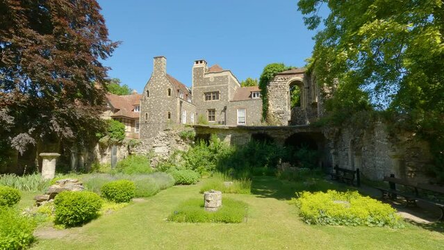 Stone walls and wooden benches surrounding herb garden with a view of old houses. A unique and peaceful aromatic corner in the courtyard of the monumental Canterbury Cathedral on a sunny summer day.
