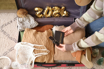 Woman packing passport, accessories and clothes into suitcase with figure 2024 made of foil...